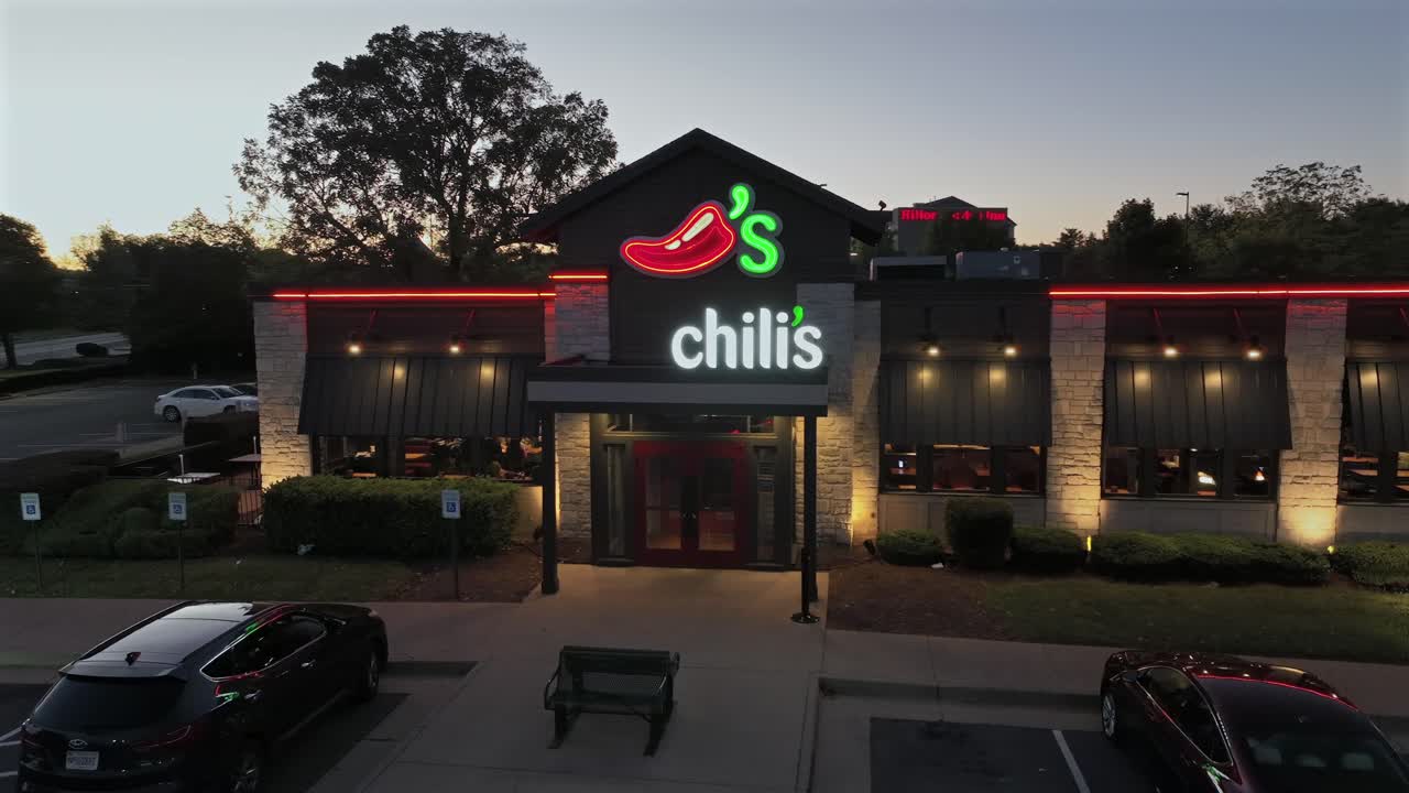 Aerial orbit shot of chilis restaurant in american town during golden sunset. Parking cars at entrance of building at Beautiful autumn day.