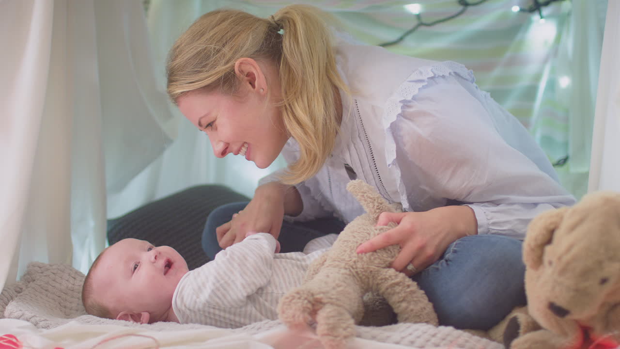 Loving mother cuddling baby son lying on rug in homemade camp in child's bedroom at home - shot in slow motion