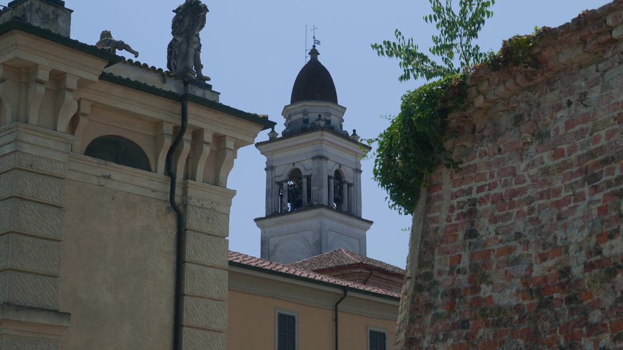 Campanile di chiesa, vista di una strada di città vecchia con facciata di architettura storica, antico muro di mattoni e cielo azzurro limpido durante una giornata di sole. Paesaggio di destinazione turistica italiana, ripresa panoramica a mano da sinistra a destra.