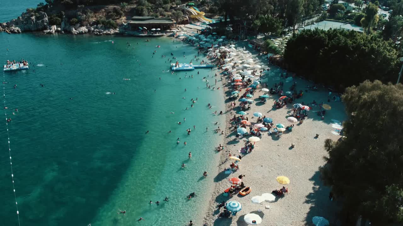 Aerial drone view showing crowded umbrellas and swimmers at Cleopatra Beach in Alanya with turquoise water, bright summer light, busy shoreline, colorful beach setup, and lively coastal atmosphere