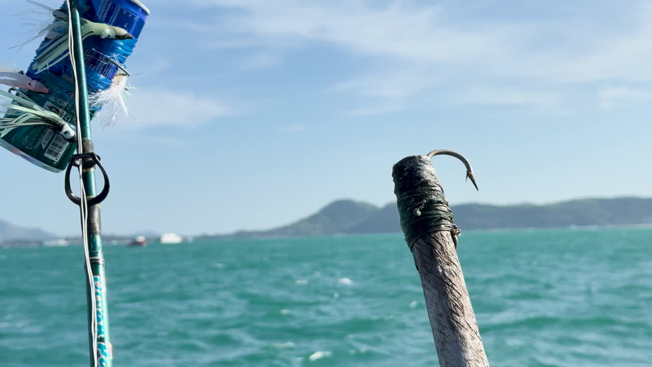A fishing rod with a recycled can lure bobs in the ocean near Phuket, Thailand, under bright daylight
