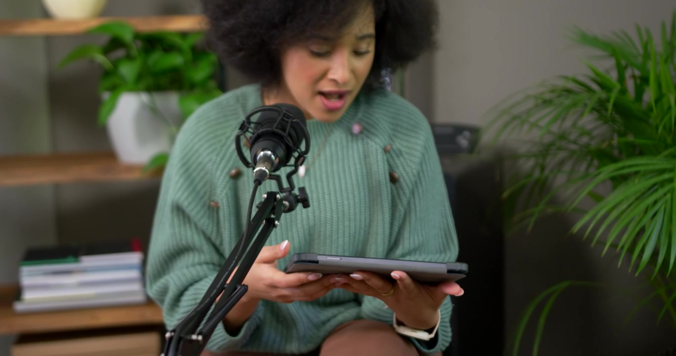 Afroamerikansk kvinde i grøn sweater læser på tablet, taler ind i mikrofon og optager derhjemme
