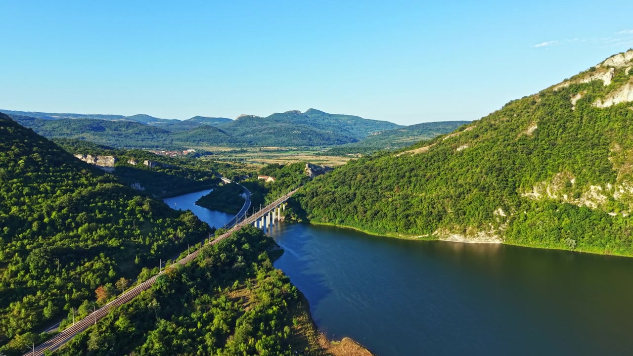 Scenic view of a river and bridge surrounded by green hills during a sunny day
