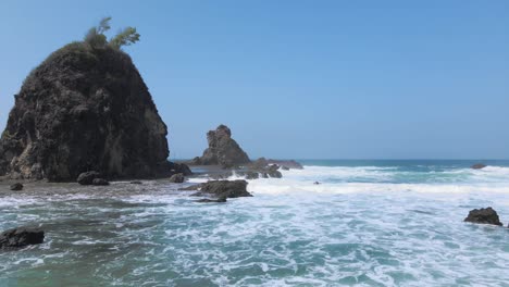 Rocky-island-and-ocean-waves-flowing-toward-shore,-aerial-view