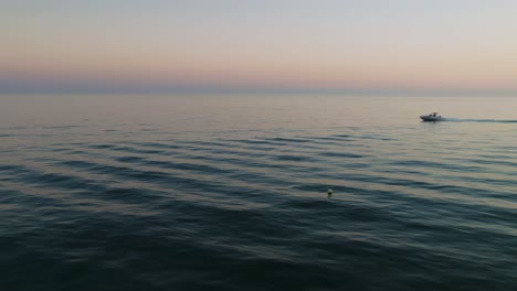 Drone-flying-over-the-sea-at-dusk-with-speedboat-passing-by