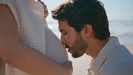 man kissing pregnant belly wife standing seashore close up. future father love