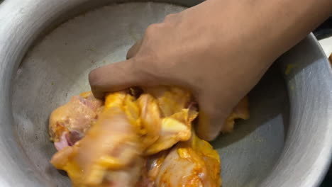 hand mixing and marinating raw chicken leg pieces inside metal bowl