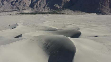 aerial drone circling left in the sand dunes of the cold desert in skardu pakistan with the rocky desolate mountains in the background on a sunny summer day