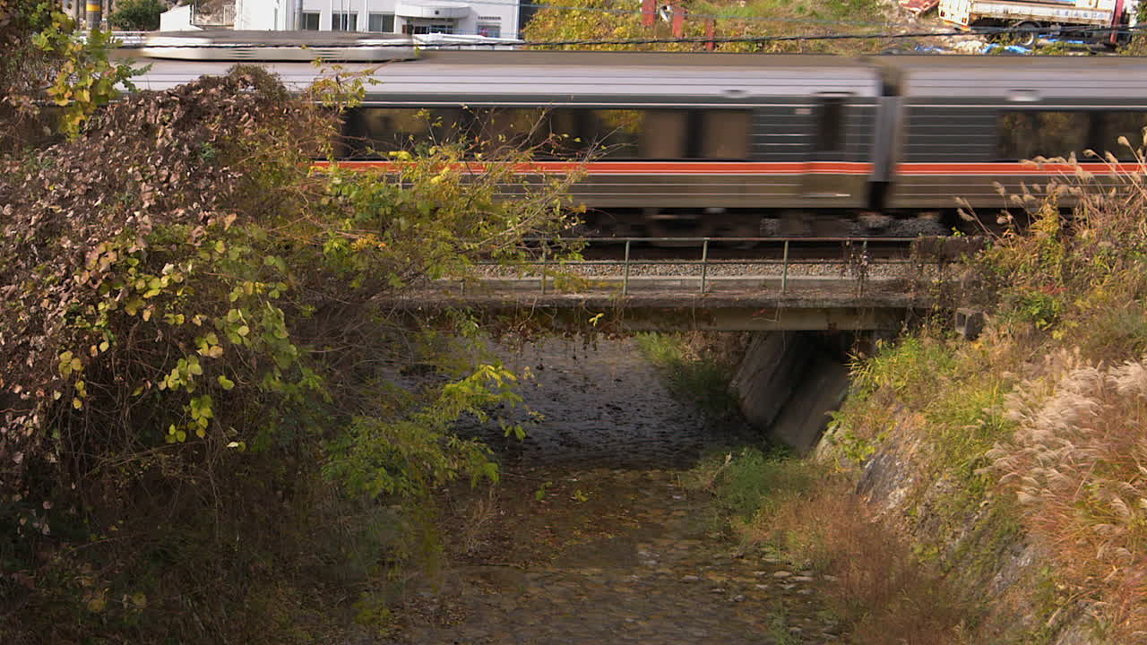 Comfortable local train crosses small creek in Japan's Nakasendo valley