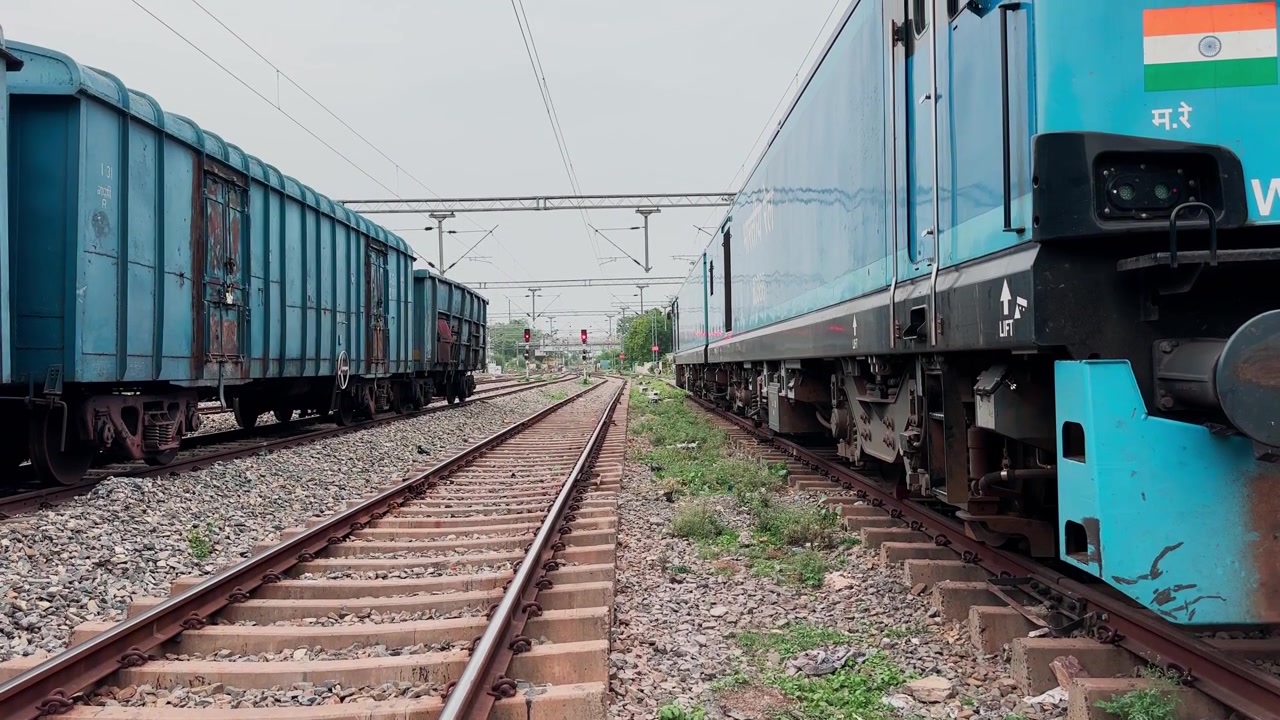 Inquadratura in elevazione che parte dai binari ferroviari e rivela una locomotiva elettrica da carico WAG-12B con vagoni merci sotto i cavi della linea aerea
