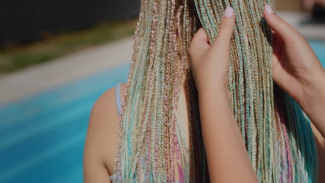A-woman-admires-her-daughter's-Afro-braids,-holds-them-in-her-hand.-Stand-by-the-pool.4k-video