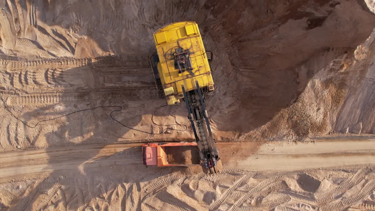 Electric rope shovel on sand mining in opencast. Mining excavator dropping rock ore into mine dump truck.