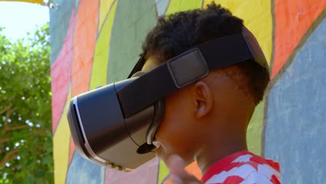 vista lateral de un escolar afroamericano usando auriculares de realidad virtual en el patio de recreo de la escuela 4k