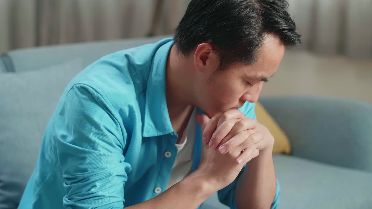 소파에 앉아서 머리를 흔들고 있는 노트북을 가진 슬픈 아시아 남자의 클로즈업