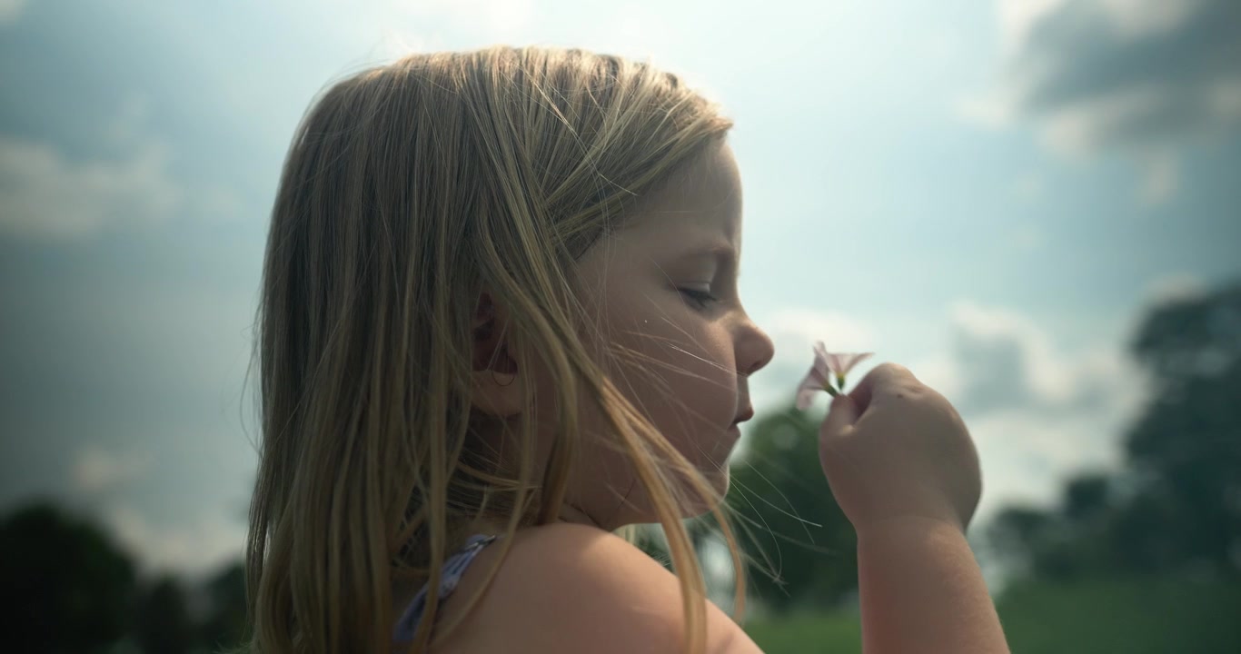 Un bambino annusa delicatamente un fiore, apprezzando la semplice bellezza della natura. Il momento è tranquillo e intimo.