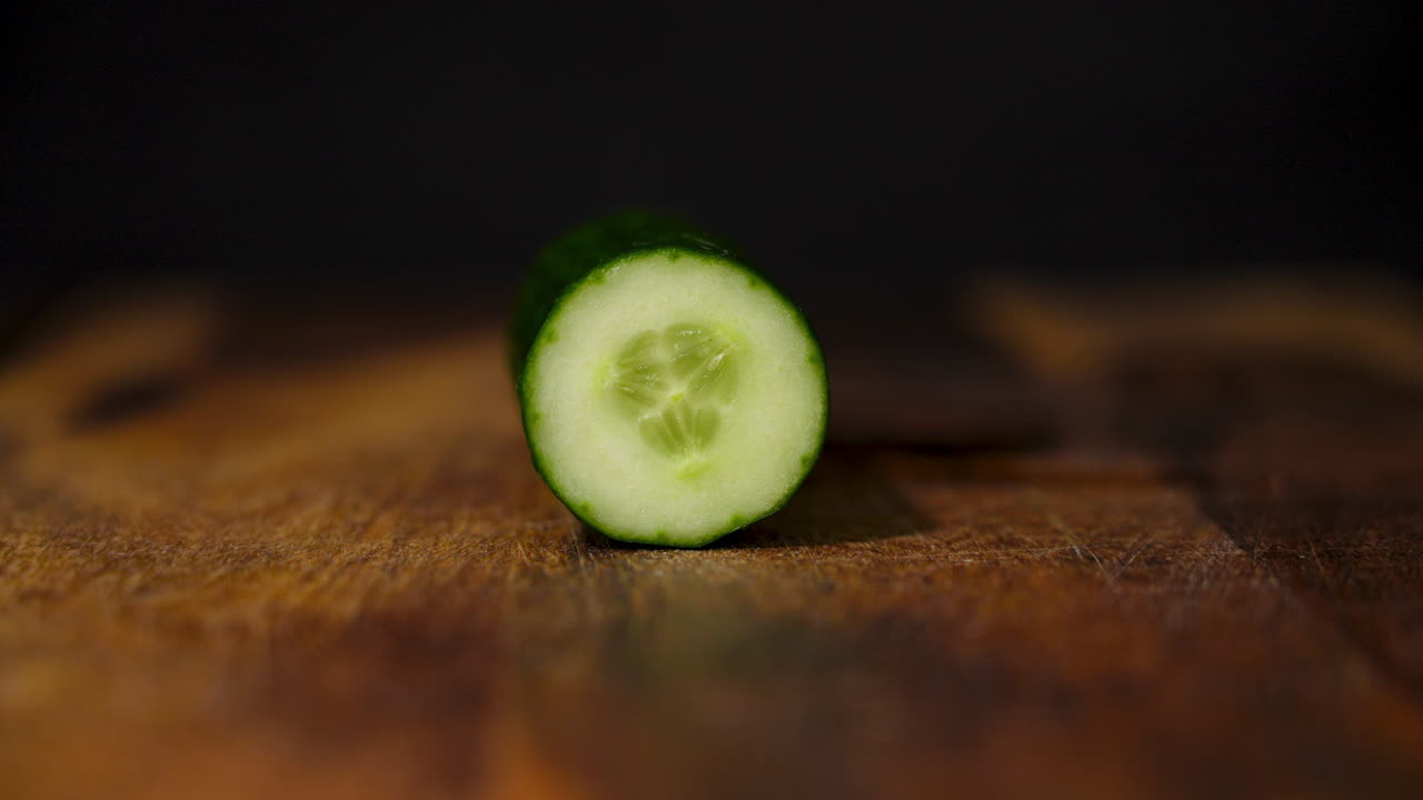 vista lateral de una mano masculina cortando un pepino fresco en una tabla de cortar de madera