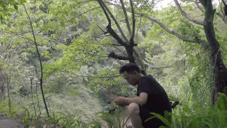 the man resting in the forest and plays with his phone