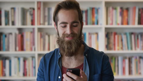 Porträt-Eines-Attraktiven-Bärtigen-Hipster-Mannes,-Der-Mit-Seinem-Smartphone-Nachrichten-Durchstöbert-Und-In-Der-Bibliothek-SMS-Auf-Dem-Mobiltelefon-Genießt.-Junger-Männlicher-Student-Recherchiert-Online-In-Zeitlupe