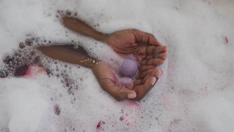 Hands-of-african-american-attractive-woman-taking-bath-with-foam,-salt-and-rose-petals