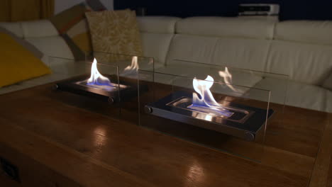 a wide shot of an indoor glass fronted fireplace in a living room on a table with a sofa in the background of the room