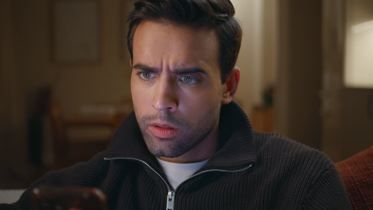 Tensed man reacting cellphone message sitting home couch at night closeup