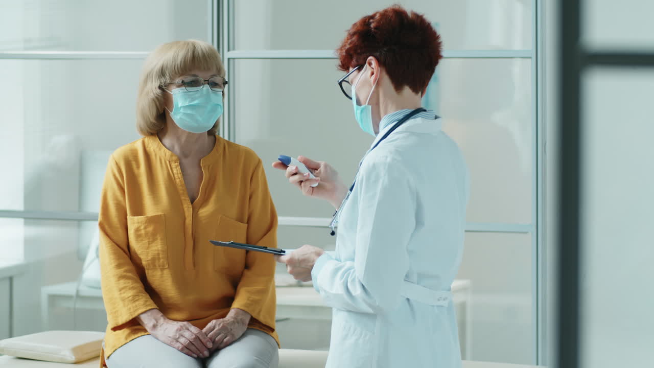 Doctor in Mask Measuring Temperature of Elderly Woman in Clinic