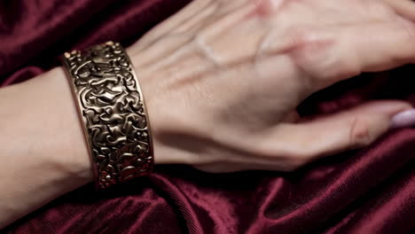 elegant gold bracelet and ring on a woman's hand with red fabric