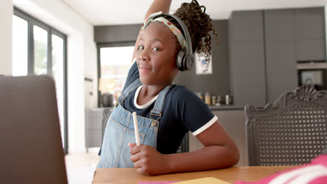 Happy-african-american-girl-using-headphones-and-laptop-rasing-hand-in-online-lesson,-slow-montion