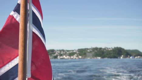 Norway-flag-blowing-in-wind-on-boat-trip-through-fjords,-closeup-view