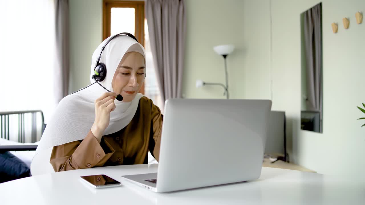 Portræt af muslimsk forretningskvinde, der arbejder med headset og bærbar computer, ser webinar, lytter til onlinekursus og kommunikerer via videokonferenceopkald, social afstand