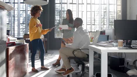 happy diverse colleagues with documents and tablets talking in sunny office, copy space, slow motion