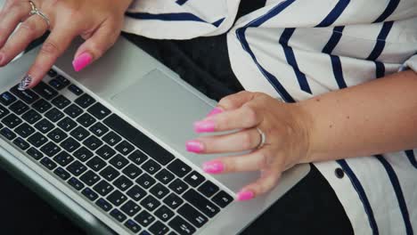 woman with stylish pink nails typing on laptop keyboard, showcasing modern workspace environment