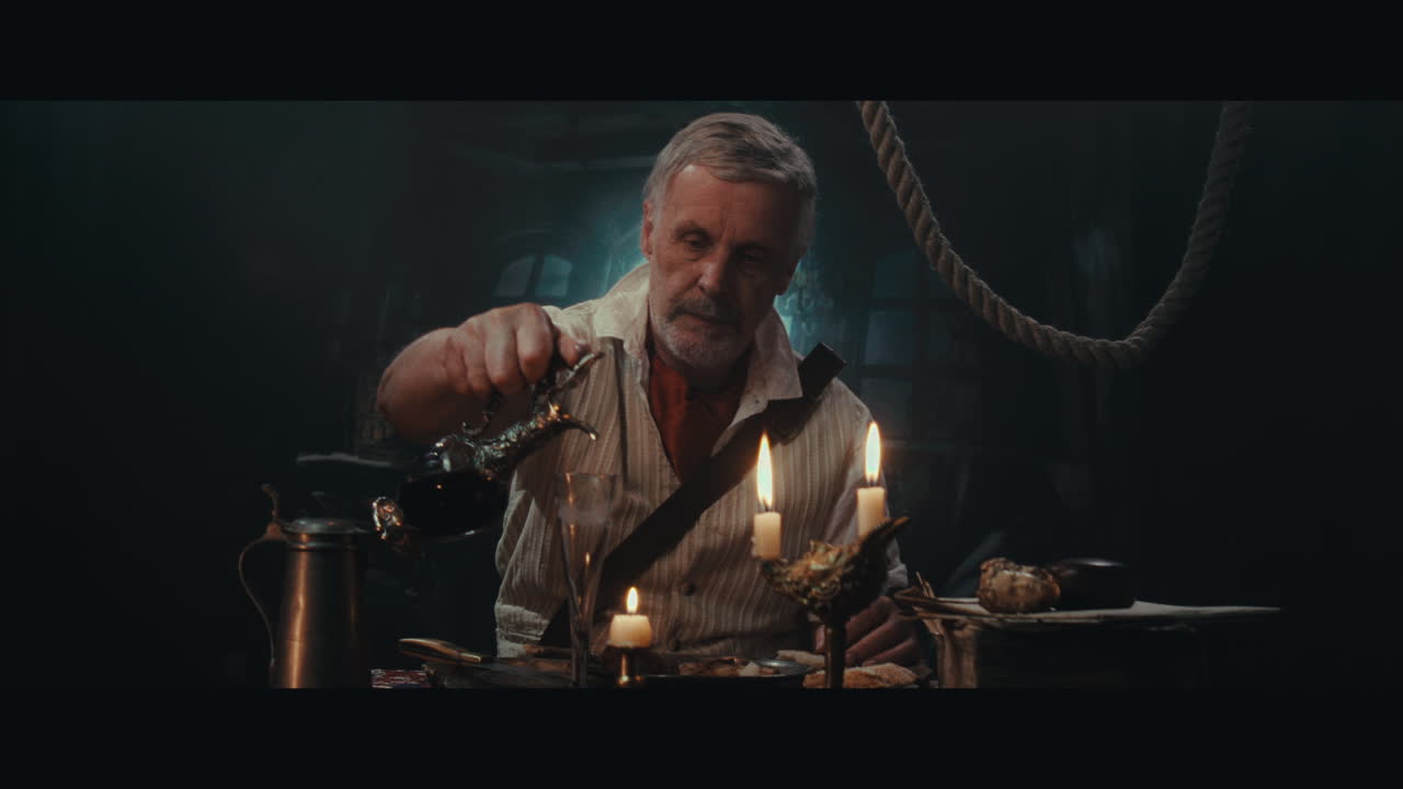 An old pirate eats and drinks inside the sailing ship cabin