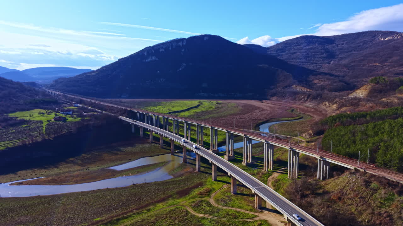 Un ponte attraversa un ampio fiume e un paesaggio con colline e campi verdi di giorno, vicino a un'area rurale