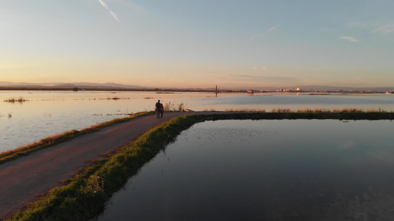 Aerial view rotating. Beautiful sunset over the rice field covered with water. Father and daughter standing on the path. Perfectly smooth surface of water in Albufera National park, Valencia Spain