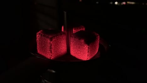 red glowing sparkling charcoals on a hookah at night. smoking hookah or shisha. the pleasure of smoking water pipe. hot red coals hookah with sparks on shisha on a dark background.