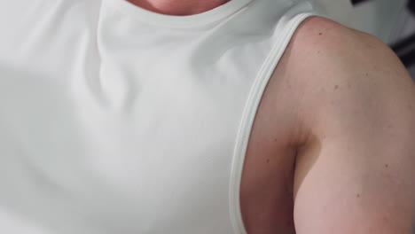 close up of male enthusiast chest and arm in white singlet straining on chest press machine muscles contracting sweat sheen controlled pushing handles with focused power for strength and endurance