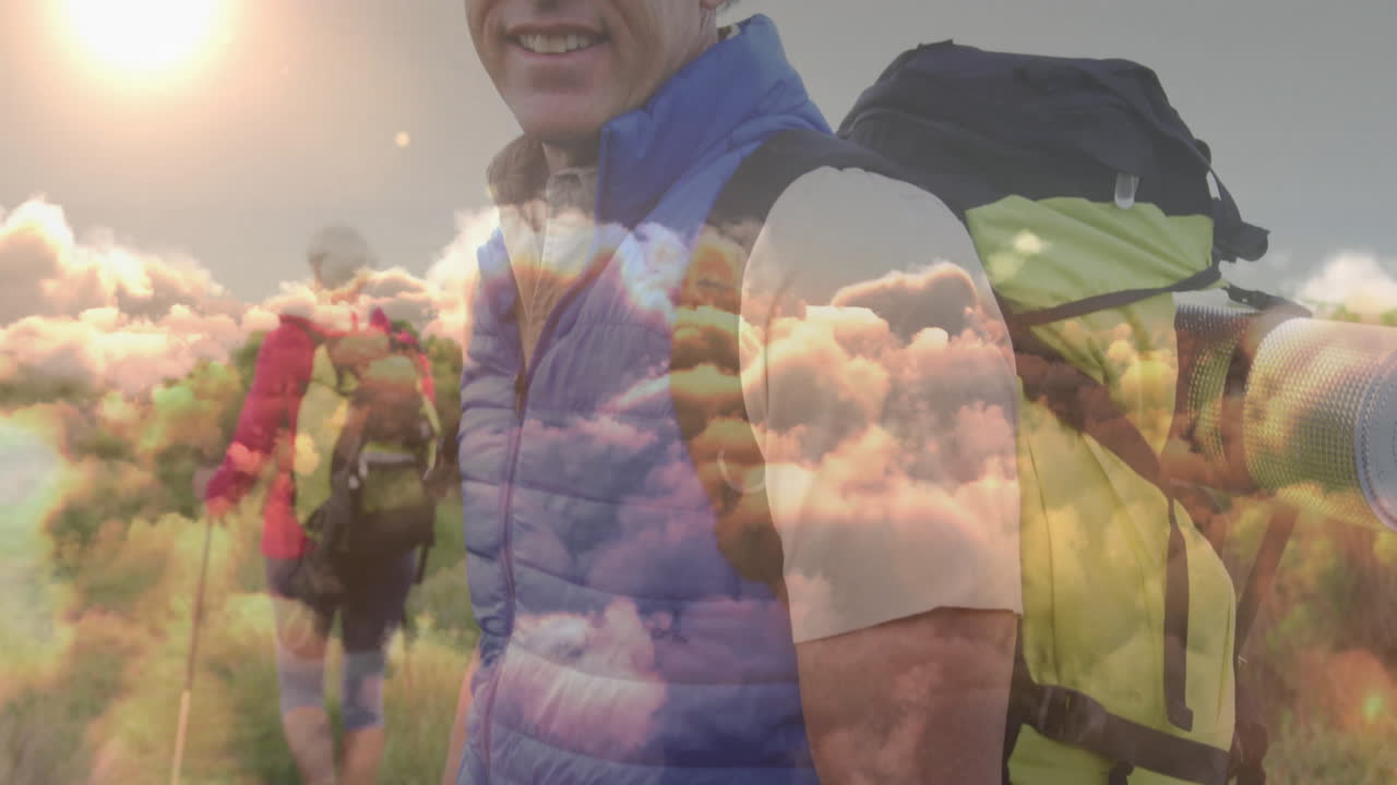 Mature man hiking with yellow backpack on grassy hillside, showing floating health data overlay