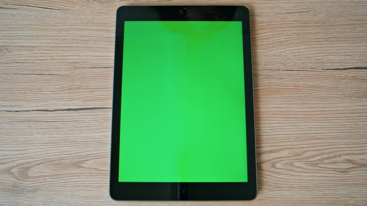 Tablet se zelenou obrazovkou umístěný v detailním záběru na povrchu dřevěného stolu. Moderní chroma key pad.