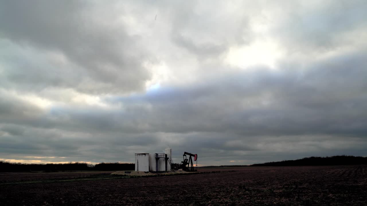 Oil field pump jack slowly pumping oil or natural gas out of the ground with storage facility. 4K UHD Extreme Wide Shot