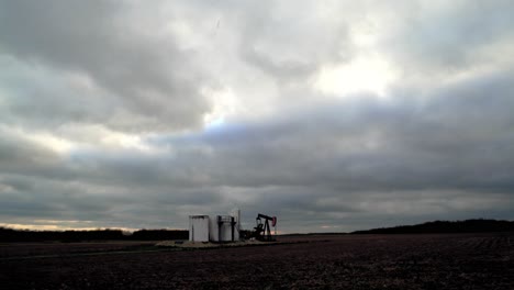 oil field pump jack slowly pumping oil or natural gas out of the ground with storage facility. 4k uhd extreme wide shot
