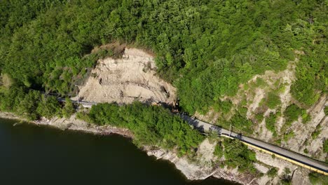 aerial image shows sp21 blocked by a recent landslide with excavators moving soil and rocks, trees and mountainside frame the disaster scene, real time drone orbiting