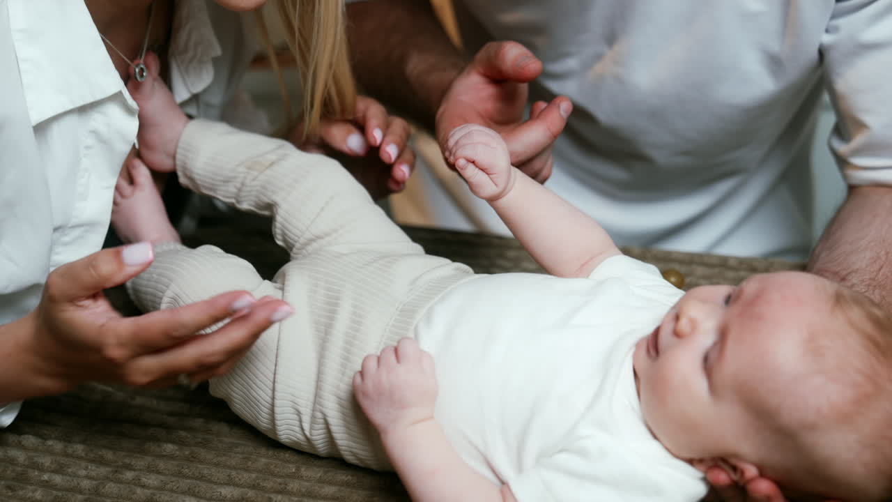 Unrecognized Caucasian parents stand near the baby lying on the plaid. Mom and dad caressing their kid.