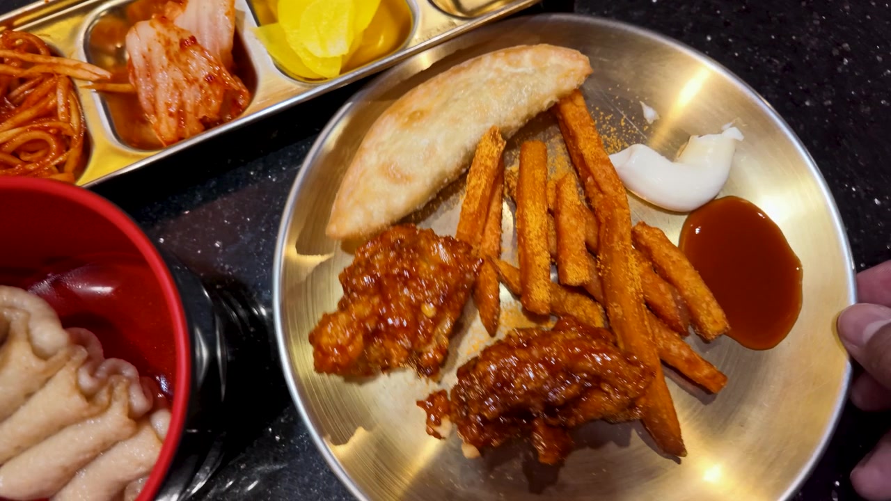 Tampak atas masakan Korea termasuk kimchi, ayam goreng, dan sate kue ikan di atas piring