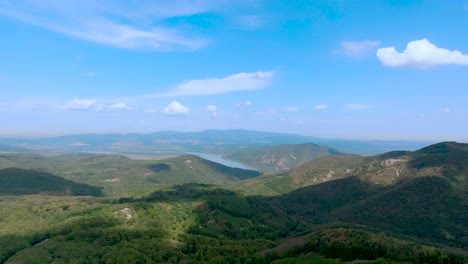 Flying-above-a-forest-on-a-sunny-and-cloudy-summer-day-under-a-blue-sky