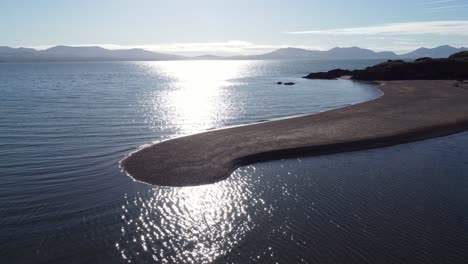 Vista-Aérea-De-La-Costa-De-Ynys-Llanddwyn-Con-Un-Océano-Brillante-Y-Una-Brumosa-Cordillera-De-Snowdonia-A-Través-Del-Horizonte-Del-Amanecer.