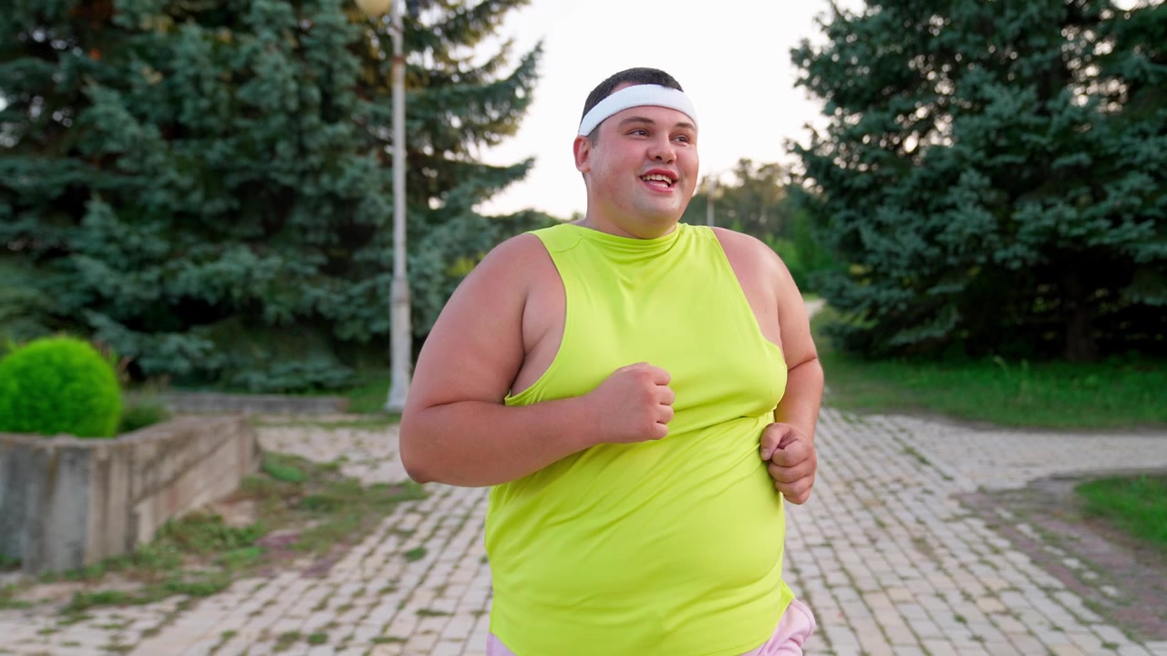 Uomo in sovrappeso che fa jogging su un sentiero asfaltato in un parco.