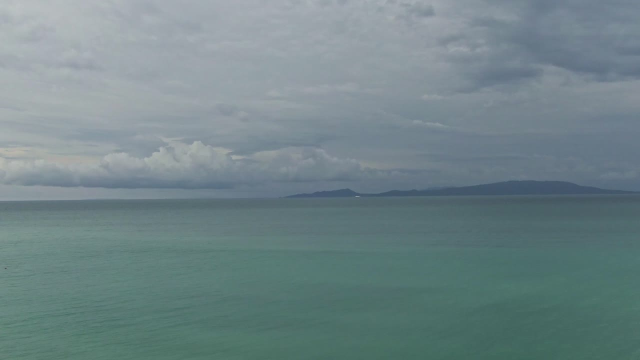 Take off view looking at the turquoise sea water , waves and the silhouetted mountain with cloudy sky above