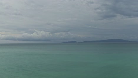 Take off view looking at the turquoise sea water , waves and the silhouetted mountain with cloudy sky above