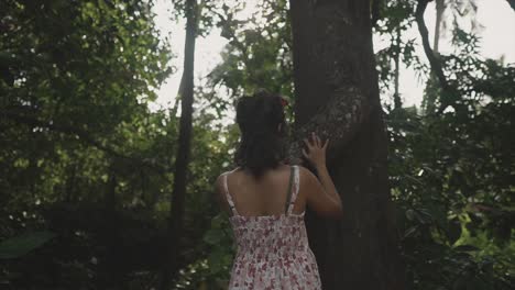 a beautiful indian girl moving her palm on a tree stem's surface in a day time in the forest